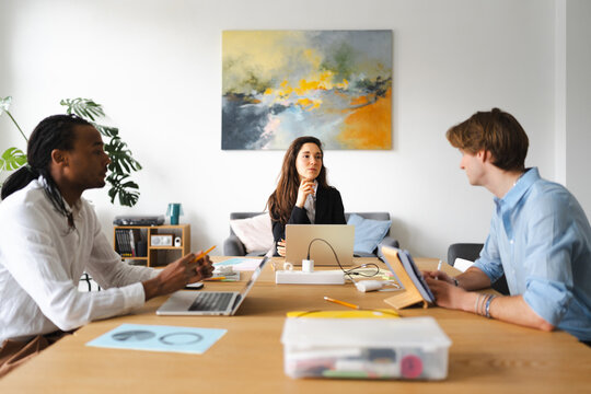 Three colleagues collaborate around a table, discussing ideas with laptops and tablets, fostering a productive work environment.