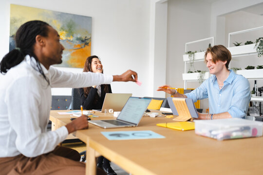 A diverse group of colleagues collaborates in a bright office space, sharing ideas and working together on projects at a shared table.