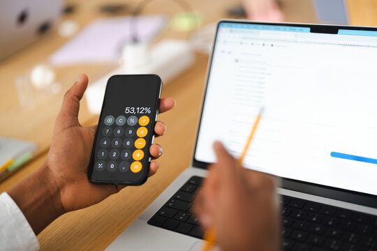 A person uses a calculator on their phone and a laptop to research information about a historical building.