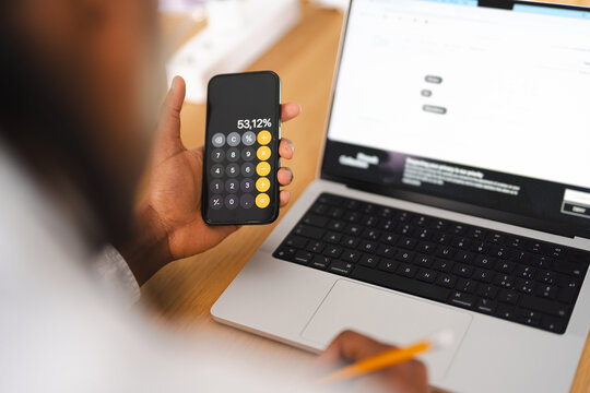 A person uses a calculator on their phone and a laptop to manage finances or conduct online research.