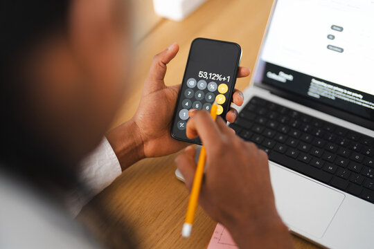 A person uses a calculator on a smartphone and a laptop for financial calculations and data analysis.