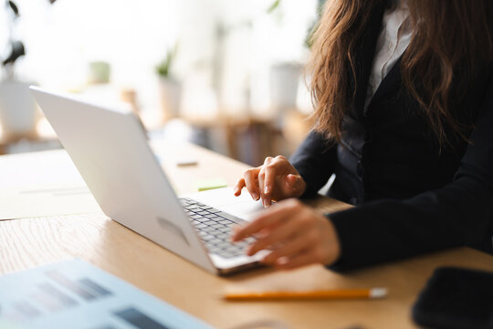 A person in a suit jacket types on a laptop, with charts and a pencil on the desk, suggesting work or study.