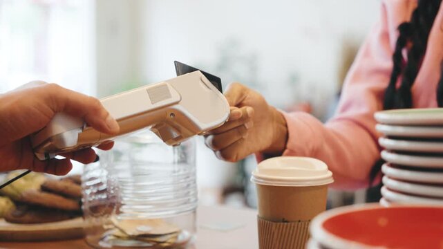 In a busy cafe during morning rush hour, a customer pays for a drink with a card through a terminal.