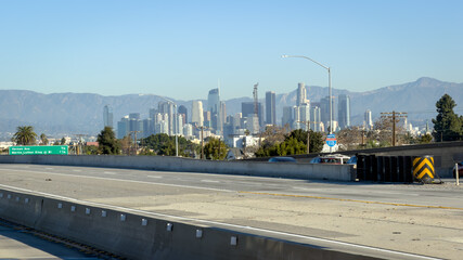 Naklejka premium Downtown LA skyline viewed from the 110 freeway with mountains behind under clear blue sky