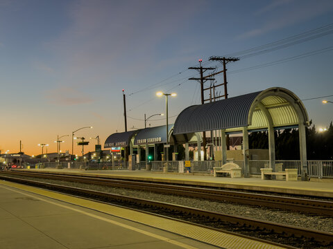 LOS ANGELES, CA, DEC 17, 2025: Bob Hope Burbank Airport Metrolink and Amtrak railway station platform at twilight, with arched metal canopies glowing against a gradient orange-blue evening sky