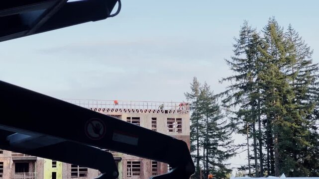 Construction site with unfinished multi story building in background and dark crane or lift arm silhouette in foreground. Residential project under construction against blue sky.