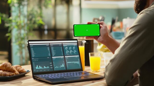 Isolated mockup on mobile phone screen used at home in kitchen, remote worker analyzing metrics and charts on laptop. Teleworking and outsourcing showing task management and research.