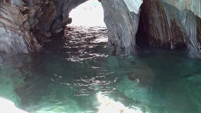 Serene journey through Patagonia's Marble Caves reveals sculpted rock walls and vibrant, clear turquoise waters. Sunlight dances on surface inside these ancient formations, showcasing nature artistry.