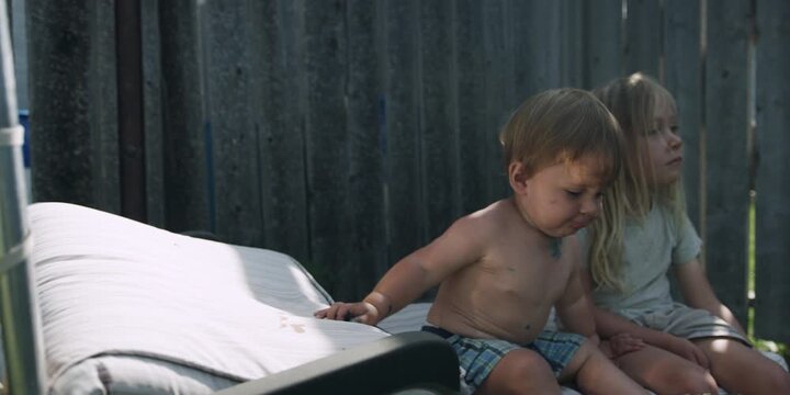 Two children on a sun lounger outdoors - boy looking at camera