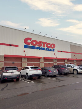 Calgary, Alberta, Canada. March 17, 2026. Exterior view of a Costco Wholesale warehouse building with cars parked in the foreground under a cloudy sky.