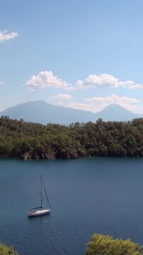 A peaceful sailboat drifts on the azure Aegean Sea, cradled by lush shores near Fethiye Oludeniz Turkey. Majestic Babadag Mountain proudly overlooks this beautiful daytime vista, under a clear sky.