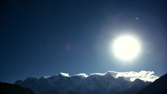 A stunning horizontal 1080p time-lapse video capturing the bright moon moving across the starry night sky over the snow-capped Namcha Barwa mountain in Tibet. Features dramatic clouds flowing over the