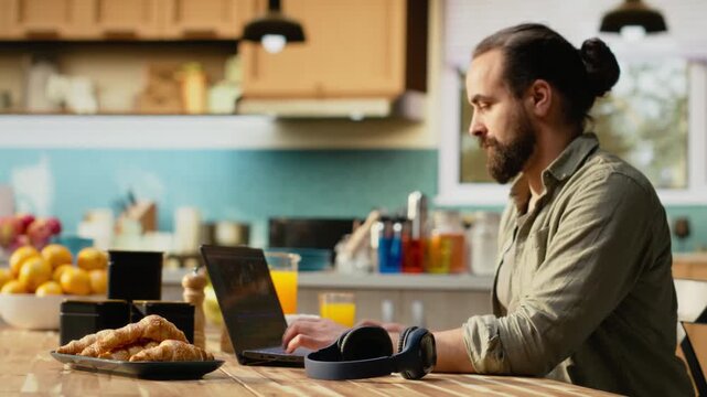 Creative editor producing cinematic footage on laptop in kitchen environment. Interactive software interface displays timeline editing, color grading and visual effects. Videography and remote work.