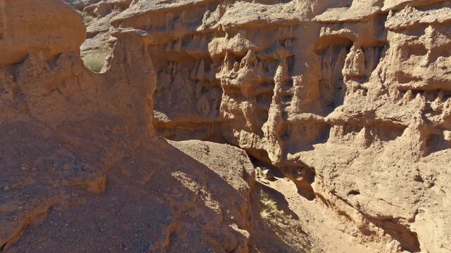 Back pulling drone view captures narrow desert canyon in Kyrgyzstan. Natural rock formations and sparse vegetation create a striking, arid landscape.