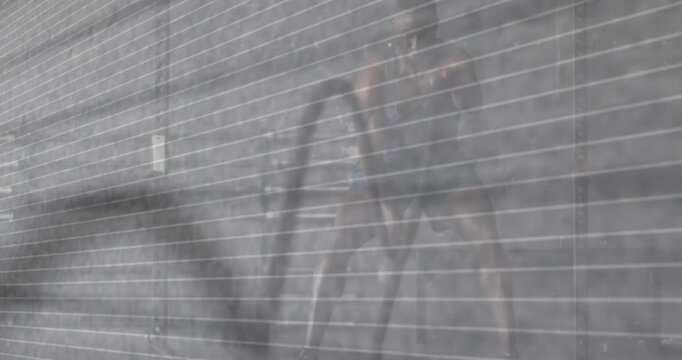 Adult man starting rope swing and widening stance, swinging rope for fitness by ribbed wall