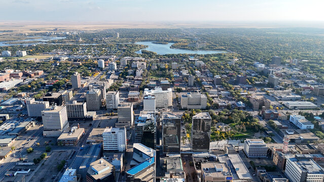 Aerial view highlighting regina's downtown core and commercial buildings with wascana lake and expansive prairie landscape stretching to the horizon under a clear sky