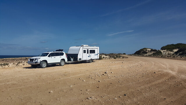 4x4 towing a caravan parked on a remote coastal road under blue sky