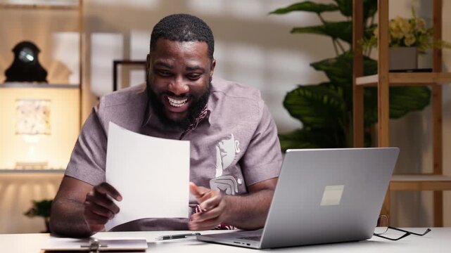 Overjoyed African businessman smiling while reading good news in a letter at his desk