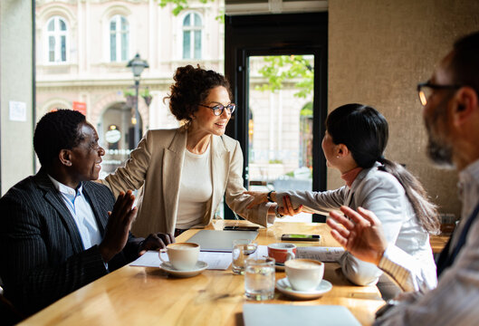 Diverse business professionals greeting with handshake in cafe