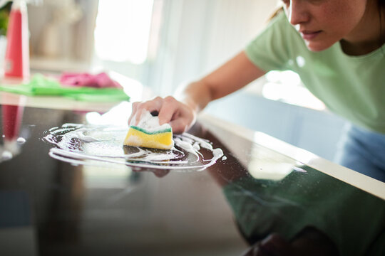 Woman scrubbing glass stovetop with sponge at home