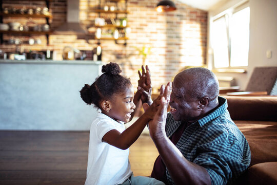 Senior man and little girl playing clapping game at home kitchen