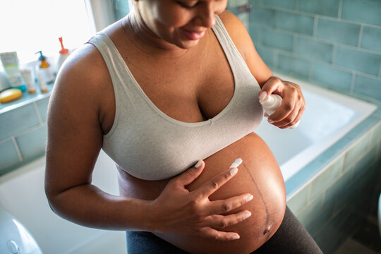 Pregnant woman applying belly cream in bathroom