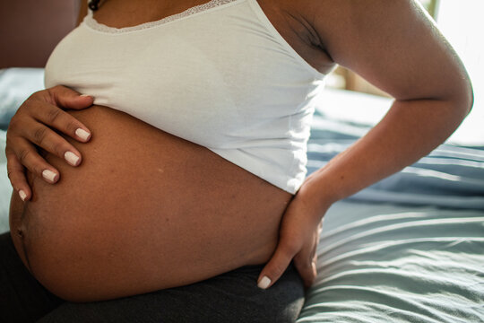 Pregnant woman cradling belly and back on bed at home
