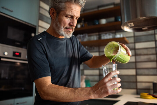Mature man pouring green smoothie in home kitchen