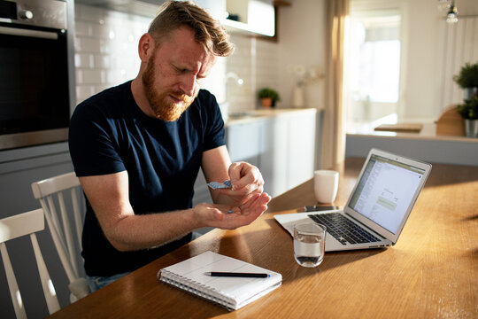 Bearded man taking medicine at kitchen table