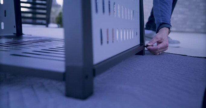 Slow motion low shot of man's hand attempting to put screw into leg of metal structure