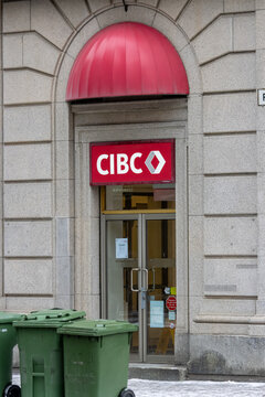 Canada, Montreal, 23 December 2025 : CIBC Bank Entrance Under Red Canopy With Green Bins Nearby