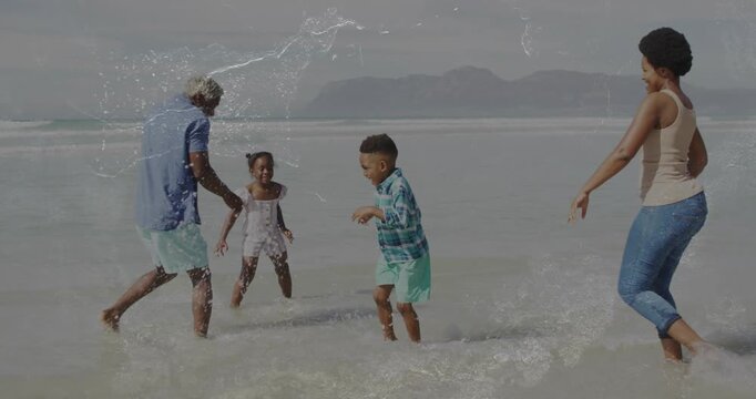 Family splashing in shallow surf, boy kicking, father splashing, mother joining for play in travel