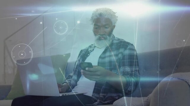 Noticing overlay graphics, middle-aged man scrolling smartphone on couch laptop open in plaid shirt