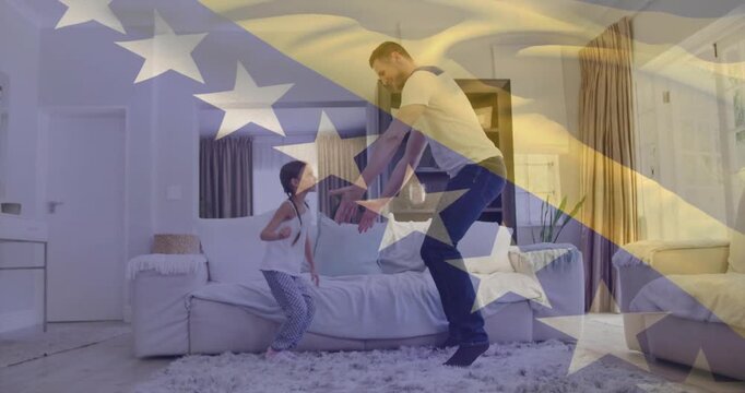 Dad bending and catching daughter stepping from sofa, guiding family hops under faint flag overlay