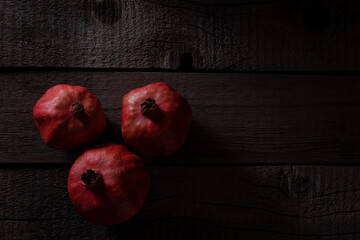Red Pomegranates on Rustic Wooden Background Captured in Dim Lighting © Erik Nurshin
