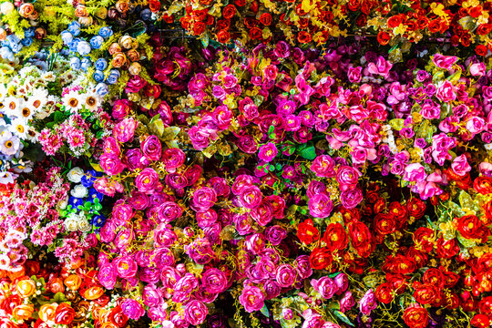 Vibrant background of dense multicolored artificial flowers and roses.