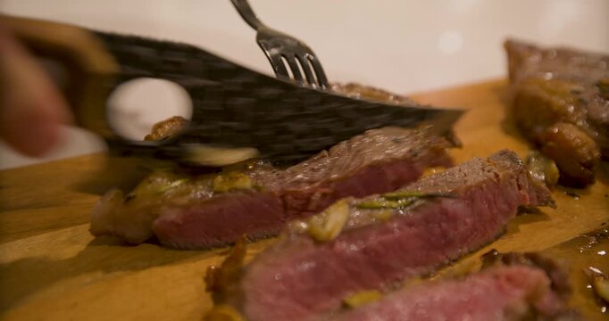 Rare steak being cut with sharp knife on wooden board in closeup shot