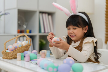 happy preschool child girl wearing bunny ears painting and decorating colorful egg at home on...