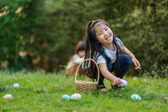 two happy child girl playing together and hunting for Easter eggs into basket on green grass in garden