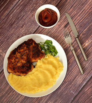 Breaded pork chop with mashed potatoes and tomato sauce on a wooden table.