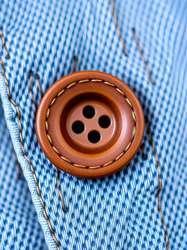 Close-up of brown button on light blue denim fabric showcasing stitched buttonhole detailing