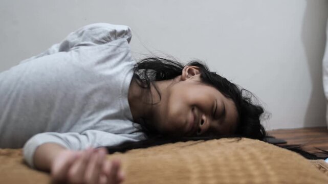 Upset little Asian girl crying and lying on bed, feeling sad and grumpy with tearful face, unhappy child sobbing or having a tantrum at home