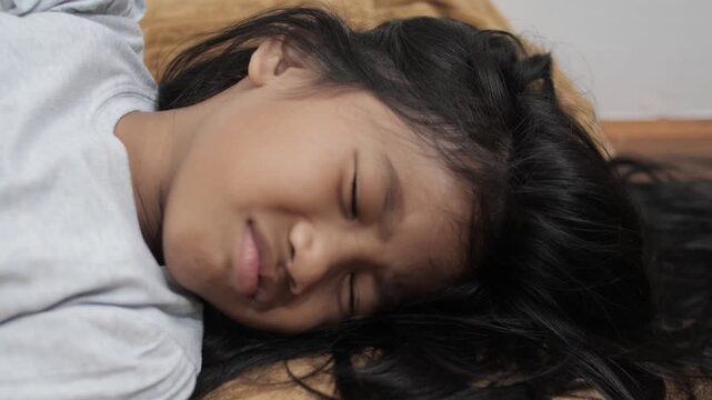 Upset little Asian girl crying and lying on bed, feeling sad and grumpy with tearful face, unhappy child sobbing or having a tantrum at home