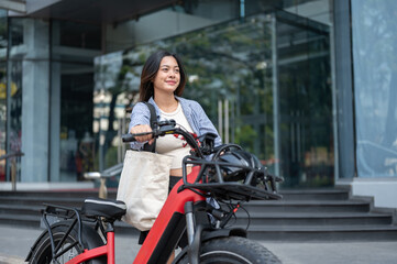 Naklejka premium Pretty asian woman walking with a fat tire electric bicycle in front of a shopping mall or building.