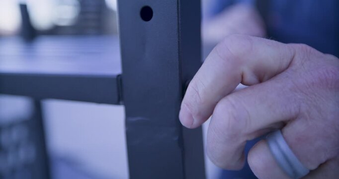 Man's hand with wedding ring turning screw into metal bar - closeup