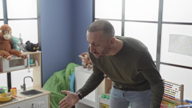Man leaning forward with palms open over toys in a kindergarten building, hands visible and speaking to child; classroom frustration.