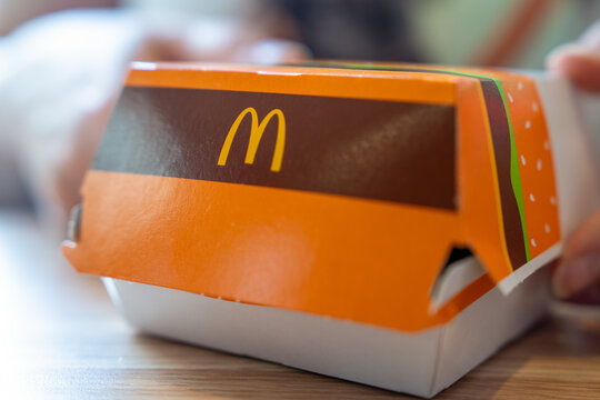 Belgrade, Serbia: July 3, 2024: Closeup of a McDonald's cardboard burger box on table, hands opening the orange package with golden arches logo visible, fast food takeaway container