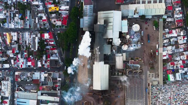 Industrial sugar mill emitting steam and pollutants into the atmosphere near a residential area