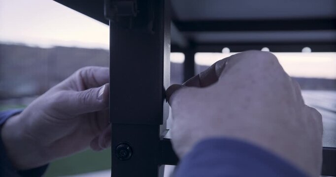Man's hands attaching bolt and screw into metal bar of structure - closeup