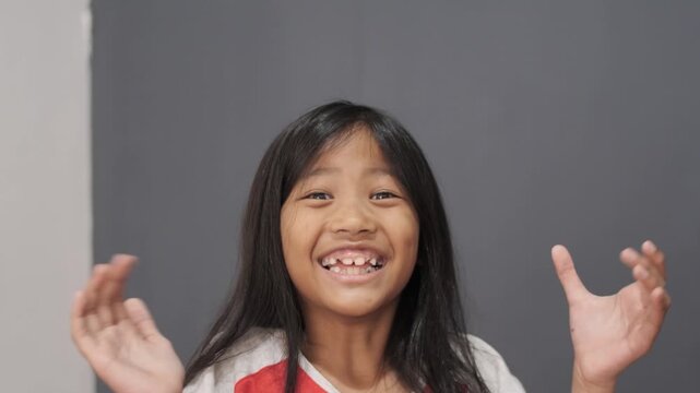 Cheerful little Asian girl clapping hands with a big smile, happy child celebrating success and feeling joyful, appreciation, achievement, and positive childhood emotion